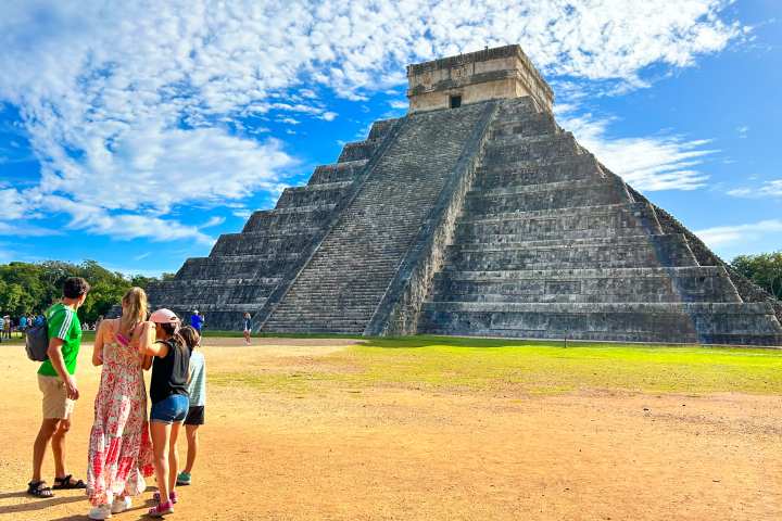 a group of people that are standing in the grass with Chichen Itza in the background