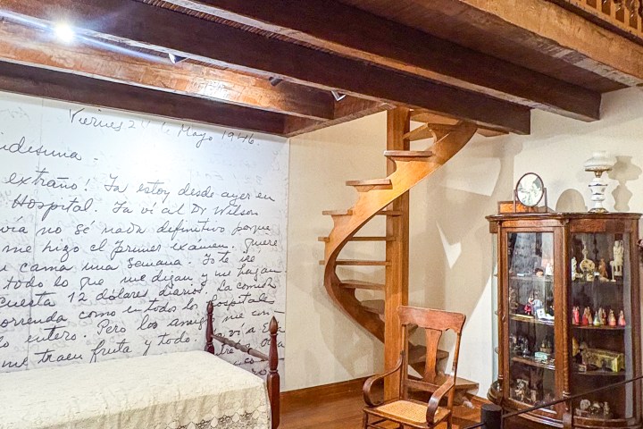 Rustic room with wooden loft, spiral staircase, bed, chair, and display cabinet.