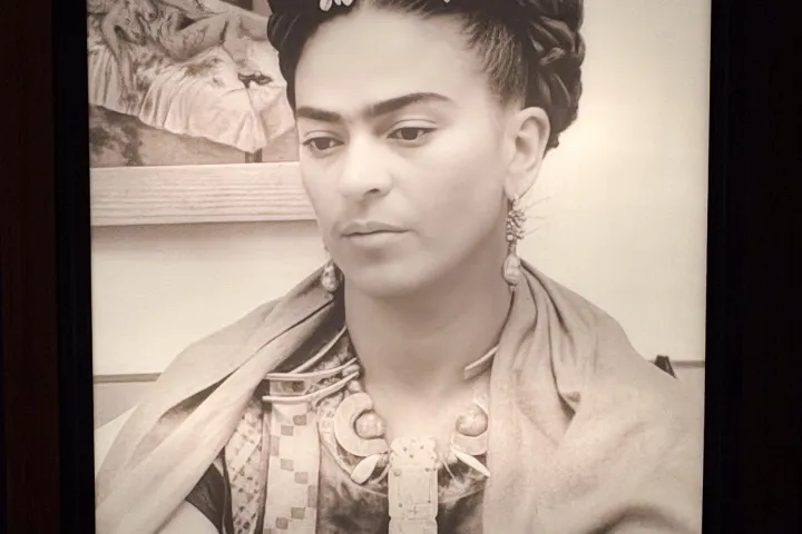 Black and white portrait of a person with flowers in braided hair, wearing earrings and a patterned blouse.
