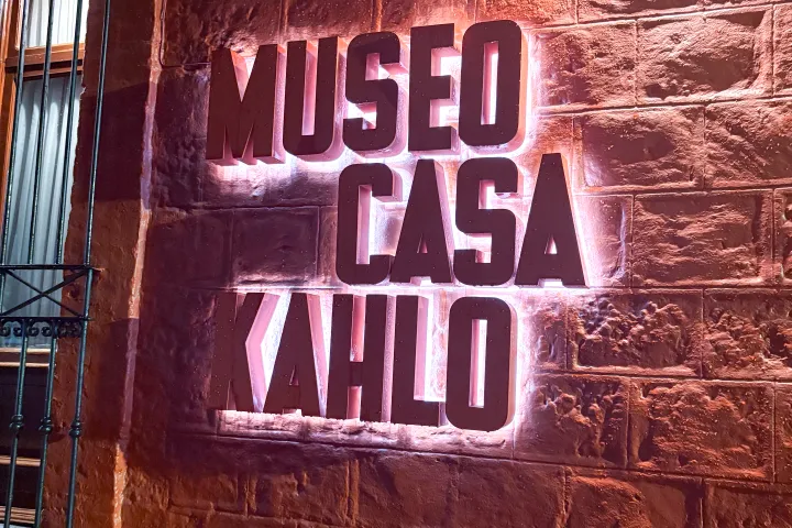 Illuminated sign reading 'MUSEO CASA KAHLO' on a textured brick wall.