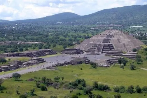 a large green field with Teotihuacan in the background