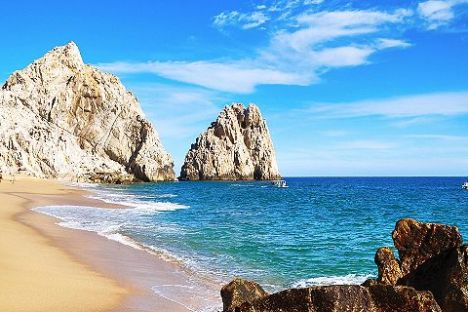 a rocky beach next to a body of water with Faraglioni in the background