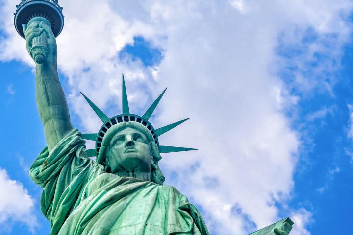 a green statue on a cloudy day with Statue of Liberty in the background