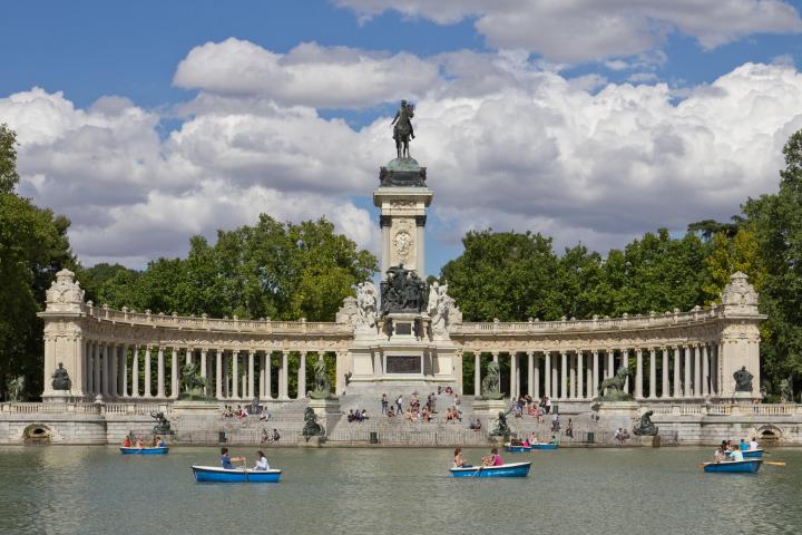a small boat in a body of water with Buen Retiro Park in the background