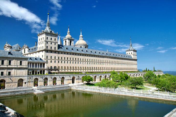 a large building next to the water with El Escorial in the background