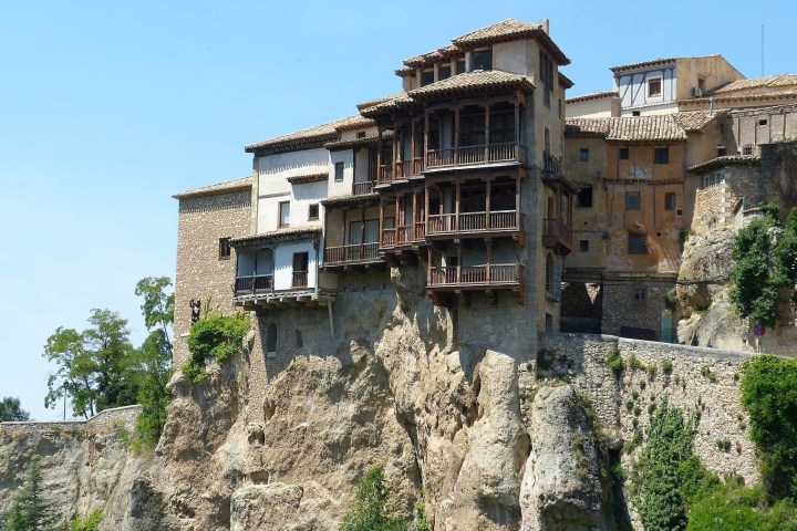 a castle with water in front of a large rock with Cuenca in the background
