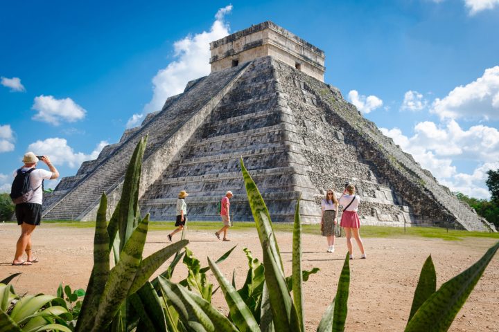 a group of people that are standing in the grass with Chichen Itza in the background