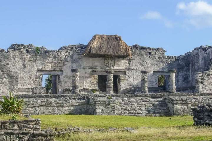 an old stone building with grass in front of a house with Wolvesey Castle in the background