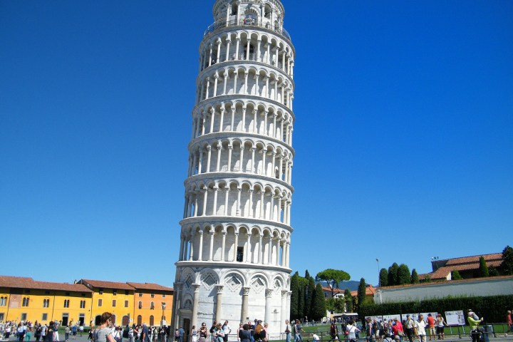 a group of people standing next to a clock tower with Leaning Tower of Pisa in the background