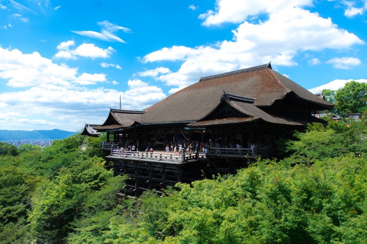 a large clock tower on top of a lush green hillside with Kiyomizu-dera in the background