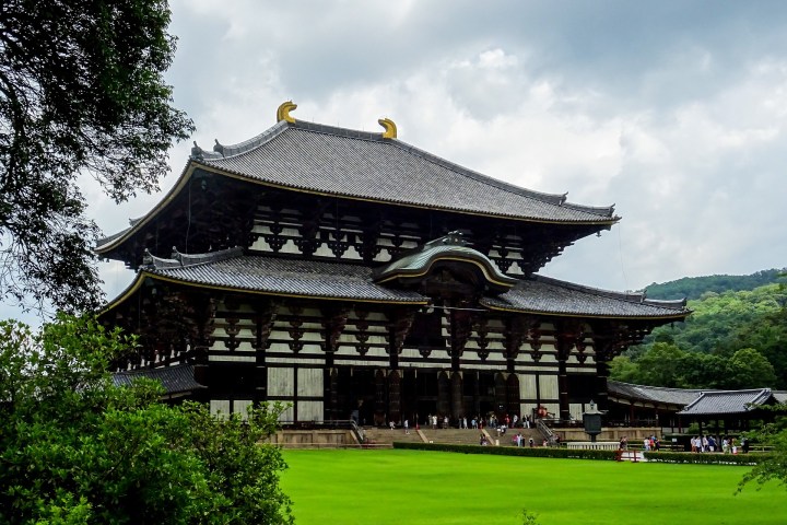 a large building with a clock at the top of a grass covered field with Tōdai-ji in the background