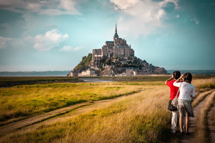 a person riding a bicycle in front of a castle with Mont Saint-Michel in the background