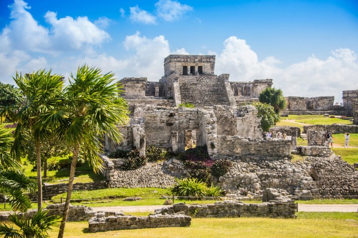 a castle on top of a grass covered field with Tulum in the background