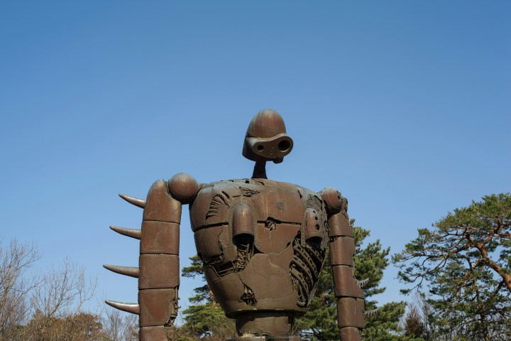 Large robot statue with spikes on arms against a clear blue sky.